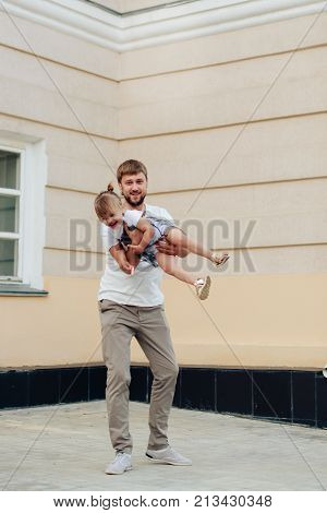 father holds little daughter in her arms on the background of the building 1