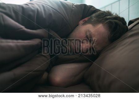 offended caucasian man lie on bed and cover himself with blanket. He is about to cry. Negative human emotion.