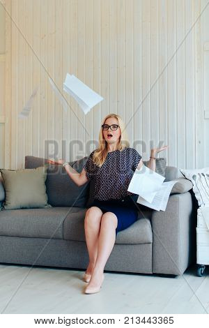 beautiful blond woman with glasses sits on the couch and throws up paper 1