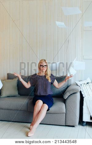 beautiful blond woman with glasses sits on the couch and throws up paper 1