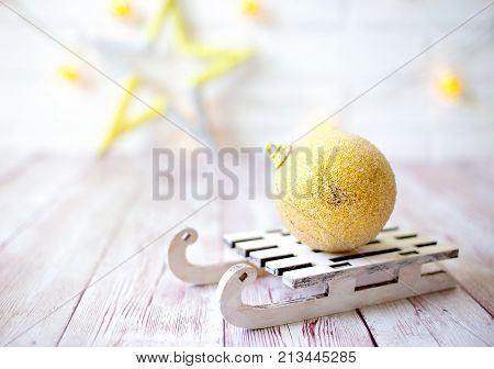 Shining Christmas Ball On Toy Wooden Sled On Light Bokeh Background With Goolden Star. New Year Card