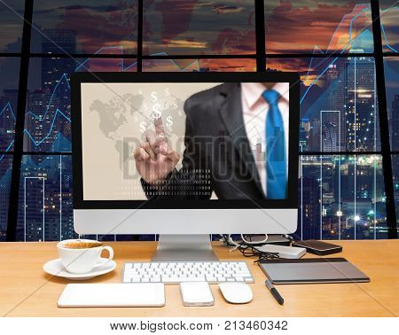 Workspace with computer desktop with Businessman point sign of money at the screen on the trading graph over the blurred photo of cityscape backgroundElements of this image furnished