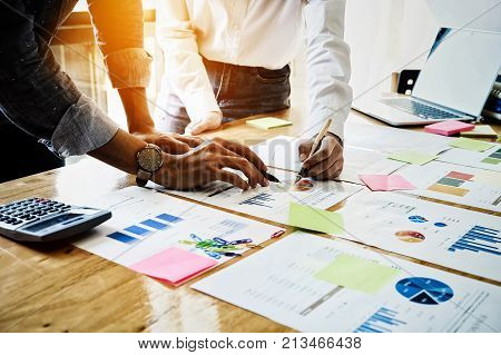 Young businessmen and partnership holding a pen pointing the graph to analyze the marketing plan with calculater and laptop computer on wood desk in office.