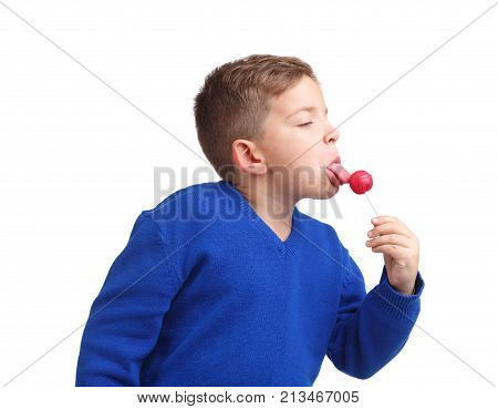 A boy in a blue sweater licks his lollipop with his tongue. Side view on white isolated background