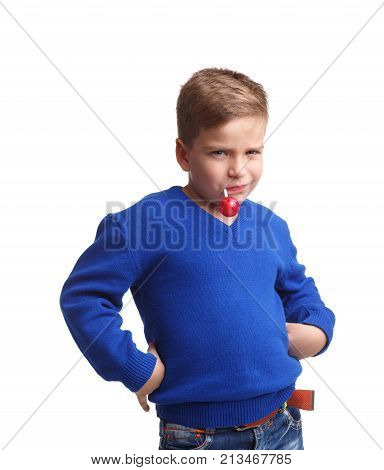 A boy in a blue sweater is holding a stick in his mouth with a lollipop. Holding his hands in the sides on a white isolated background