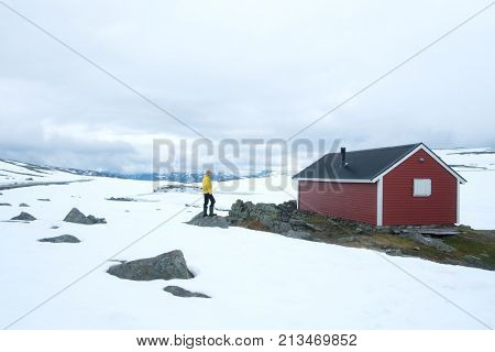 Man near typical norwegian red wooden house near famous Aurlandsvegen (Bjorgavegen) mountain road in Aurland, Norway in summer time