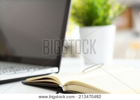 Silver pen lying on opened notebook sheet closeup in office with laptop pc on worktable. Inspector occupation for student examination or career strategy personal training course signature concept