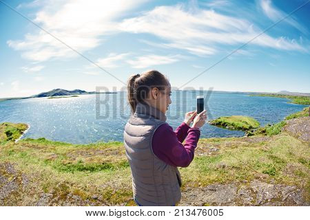 back view of woman on the shore of tne Thingvallavatn lake in Thingvellir National Park, largest natural lake in Iceland. Travel to Iceland. woman taking photo on phone