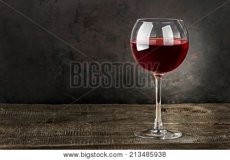 Glass of red wine on a wooden table. Dark blurry background.