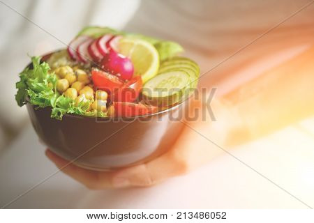 Girl in white jeans holds in hands fork, vegan breakfast meal in bowl with avocado, quinoa, cucumber, radish, salad, lemon, cherry tomatoes, chickpea, chia seeds. Top view, copy space. Clean eating.