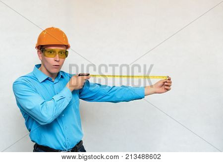 Young builder worker holding in hands construction roulette and measures copy space isolated. Engineer takes measurements.