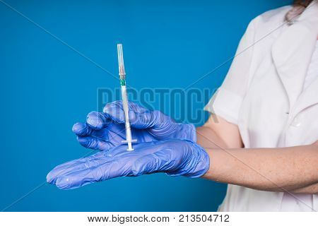 female doctor in white medical dressing gown and blue gloves holds a syringe in hands