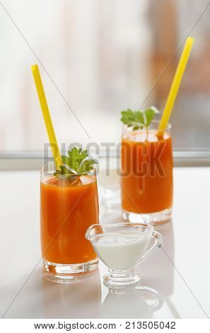 Two glasses of fresh carrot juice and cream stand on the windowsill