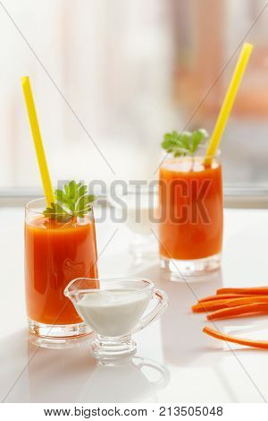 Two glasses of fresh carrot juice and cream stand on the windowsill