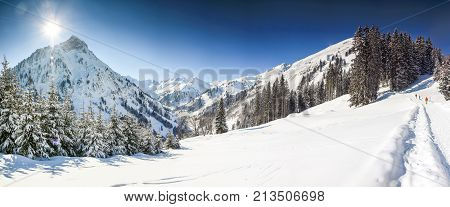 Three people hiking in mountains winter landscape with deep snow on clear sunny day. Alps, Bavaria in Germany.