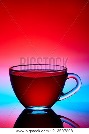 Two cups and saucers of glass. Tea is poured into the top Cup. Helium filter gives a beautiful light. Studio photos using the backlight. The reflection on the black table. The background is orange-red.