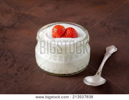 White yogurt in glass bowl with spoon and starwberries on rustic background.