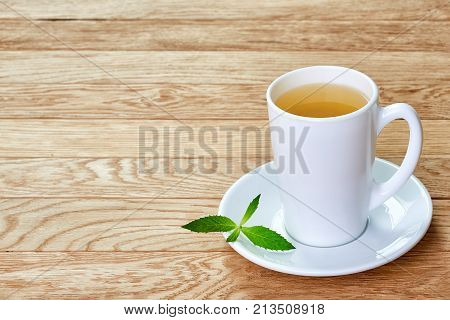 Tea with lemon in white cup, cinnamon sticks, knitted woolen scarf on a wooden table
