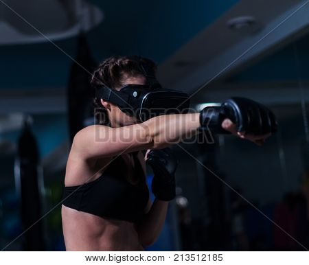 Young fighter boxer fit girl in VR glasses wearing boxing gloves in training punching unreal enemy in real life. Boxing game in virtual reality 360 degrees. Futuristic gaming