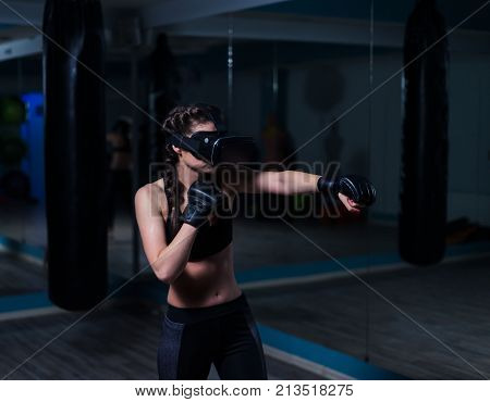 Young fighter boxer fit girl in VR glasses wearing boxing gloves in training. Boxing game in virtual reality 360 degrees. Futuristic gaming