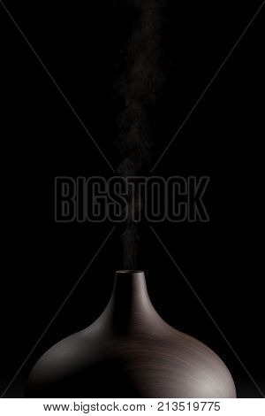 Aromatherapy diffuser. Modern electric essential oil atomizer in use. Close up against black background.