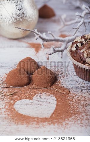 Homemade dark chocolate truffles with heart shaped cocoa powder and winter decoration on white rustic wooden table. Winter holiday background.
