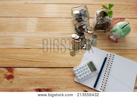 Coins in  jar for money saving and Plant Growing In Saving Coins jar for Investment  concept with calculator,note,pencil on wood board,money planning for future,top view