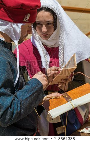 Medieval reenactors in scribe costumes practicing traditional illumination writing calligraphy with feather quill and ink, Mdina, Malta, April 2017