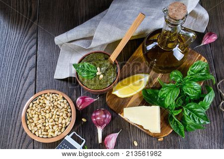 Tradizione Italiana Homemade Pesto recipe ingredients on dark table. Parmesan cheese basil leaves pine nuts olive oil garlic.
