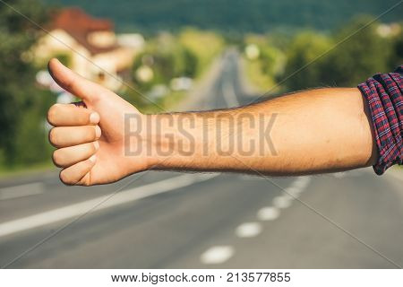 Hitchhiker sign on road. Thumb up male hand gesture outdoors. Hitchhiking hitching thumbing auto stop concept. Travel trip vacation wanderlust.