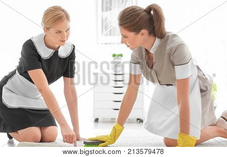 Chambermaid teaching trainee to clean carpet in room