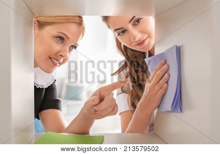 Chambermaid teaching trainee to clean shelf from dust