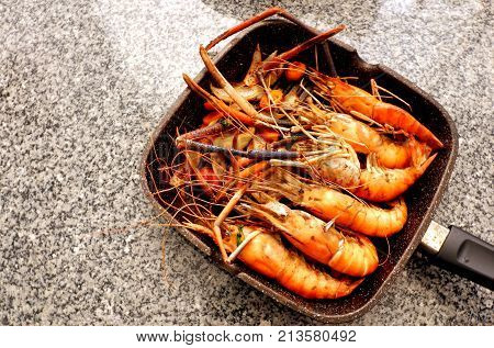 Grilled shrimp on flying pan on black stone background,top view