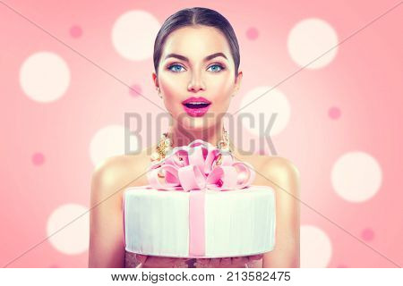 Beauty fashion model girl holding Beautiful Big Cake. Funny joyful styled woman with wedding, party or birthday cake on pink background. Diet, dieting concept. Junk food, Slimming, weight loss