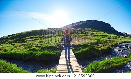 back view of woman traveler with small orange backpack on a walk in the Valley of the river of Hveragerdi Iceland. Hiking Tour of Reykjadalur Hot Springs