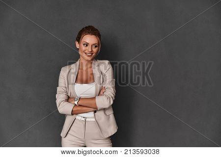Modern businesswoman. Attractive young woman in smart casual wear keeping arms crossed and smiling while standing against grey background