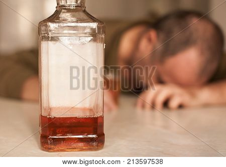 Alcohol addicted man sleeping at the table. Sad depressed male adult having troubles with alcohol.