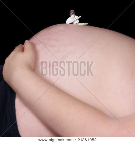 Chupeta descansando em cima de uma barriga de grávida nua. Isolado