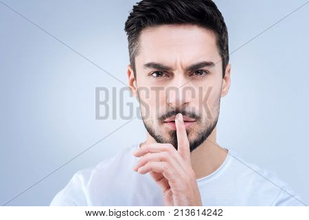Quiet. Calm professional young teacher pressing his finger to the lips while asking his pupils to be quiet at the lesson