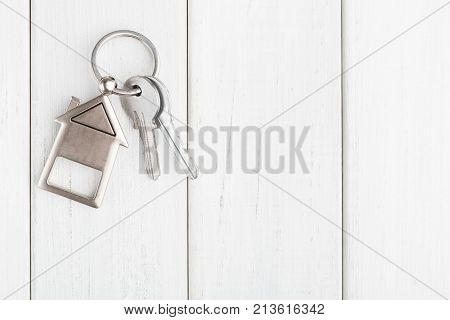 Two steel keys with house shaped trinklet on keyring on white wooden background with copy space. Home key, safety, security, real estate and rent concept, top view