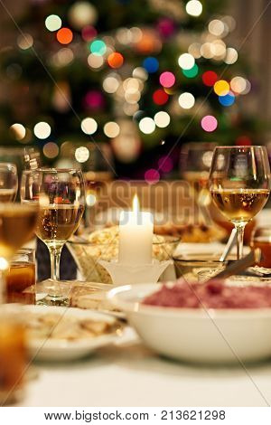 Warm mood around dining table full of a variety of delicious festive food and wine with a Christmas tree in the background
