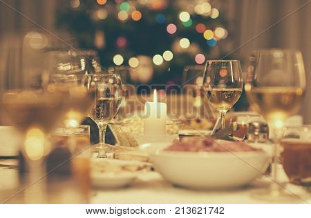 Dining table full of a variety of delicious festive food and wine with a Christmas tree in the background in home with vintage style