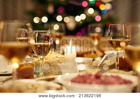 Warm dining table full of a variety of delicious festive food and wine in home with a Christmas tree in the background