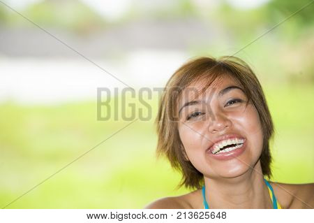 close up portrait of young happy and beautiful expressive Asian woman laughing excited and nice in positive face expression and happiness concept outdoors with copy space