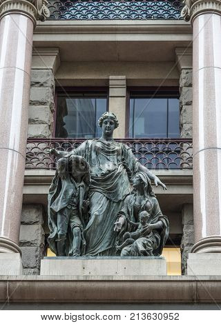 Sydney Australia - March 25 2017: Charity themed bronze statue of young strong woman consoling mother with teenaged boy and baby against facade of historic building.