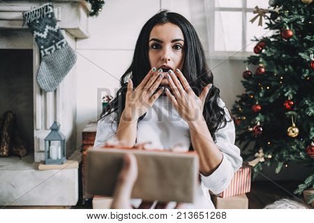 Emotional picture of a beautiful girl getting a present. She is sitting on white furry carpet and looking straight to the camera. It is so unexpected for her to get a present. She is really amazed. Cut view
