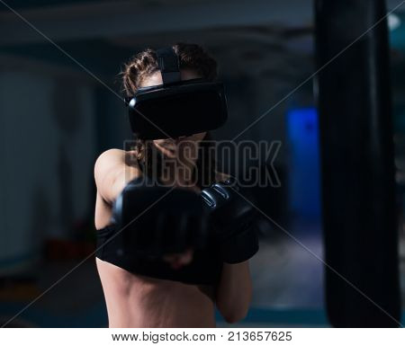 Young fighter boxer fit girl in VR glasses wearing boxing gloves in training. Boxing game in virtual reality 360 degrees. Futuristic gaming in real life