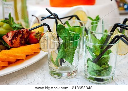 Fresh fruits and berries of different bright colors cut in small pieces are served on a table with mohito cocktail