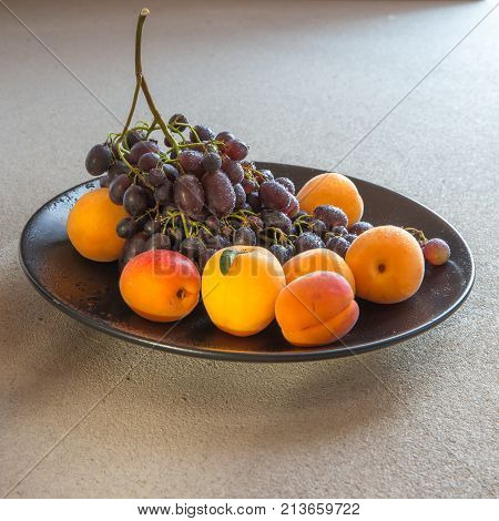 Fruit plate with grapes, apricot and almond on black plate and gray background
