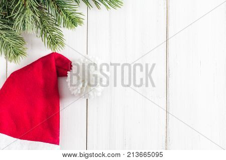 Christmas fir tree branches with santa claus hat on white rustic wooden background with copy space for text